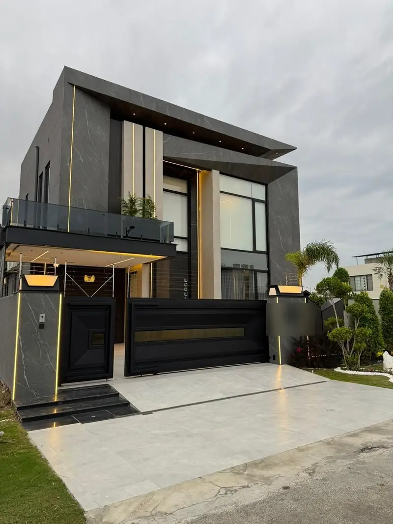 Modern two-storey house with grey marble-effect cladding, warm LED strip lighting, glass balcony and black sliding gate