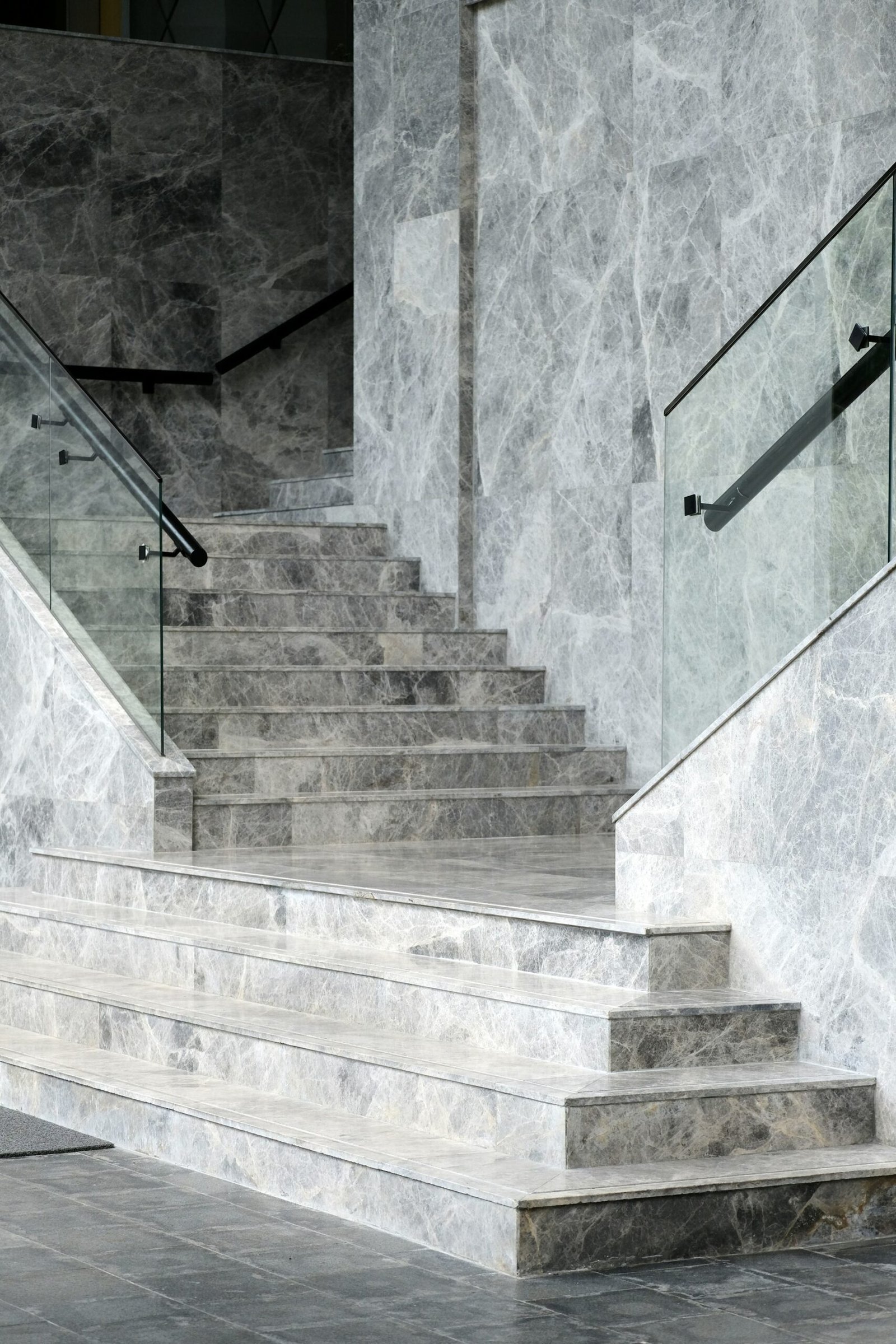 Staircase finishing in grey marble with glass railing and steel handrail